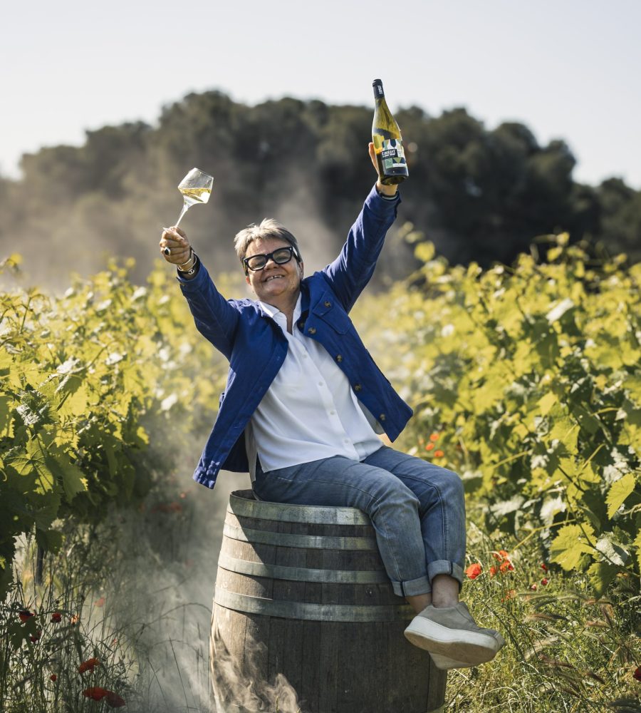 Brigitte jeanjean dans les vignes avec une bouteille de vin blanc l'inedit